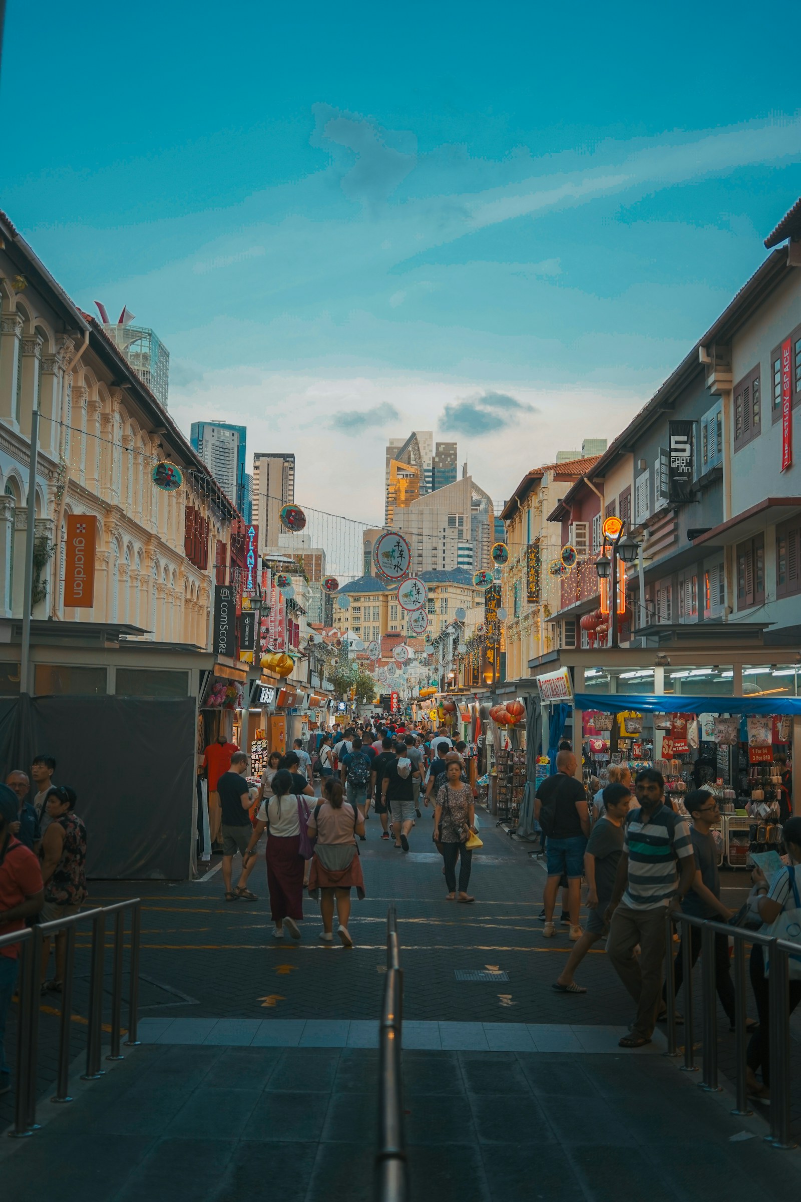 Pedestrian street in Singapore Chinatown with shophouses, stalls, and city towers at the far end